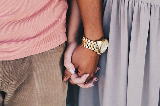 Man wearing a pink shirt holding hands with his partner.