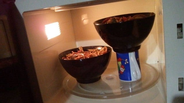 A bowl elevated over another bowl using a cup, so that two bowls can fit in the microwave