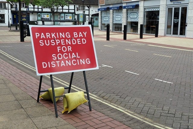 A red roadwork sign in a parking space that says ‘parking bay suspended for social distancing’