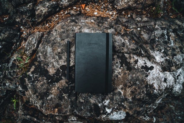 A leather-bound journal and pen placed outside on top of a large mossy rock.