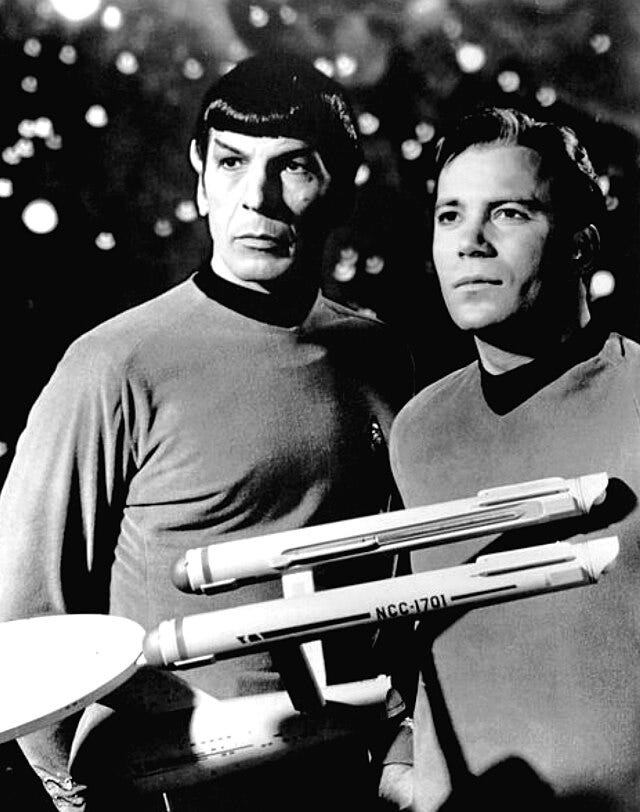 Vintage black and white photo of Captain Kirk and Mister Spock from Star Trek TOS with a model of the star-ship Enterprise in the foreground. Source Wikimedia Commons.