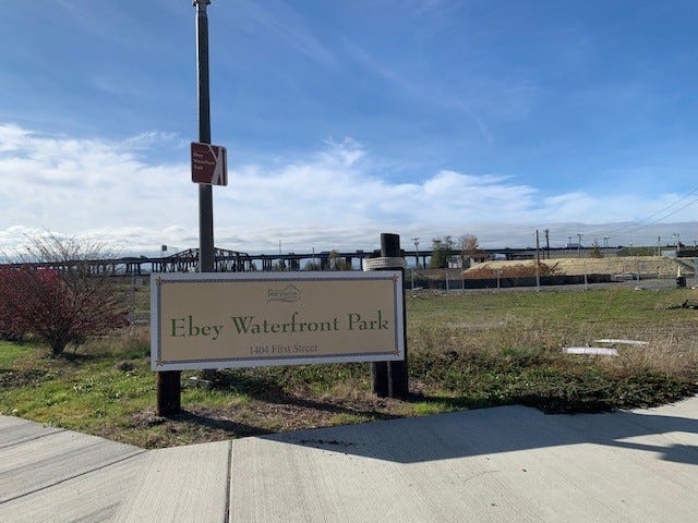 Photo of the sign for Ebey Waterfront Park, with the park in the background and bridge in the distance
