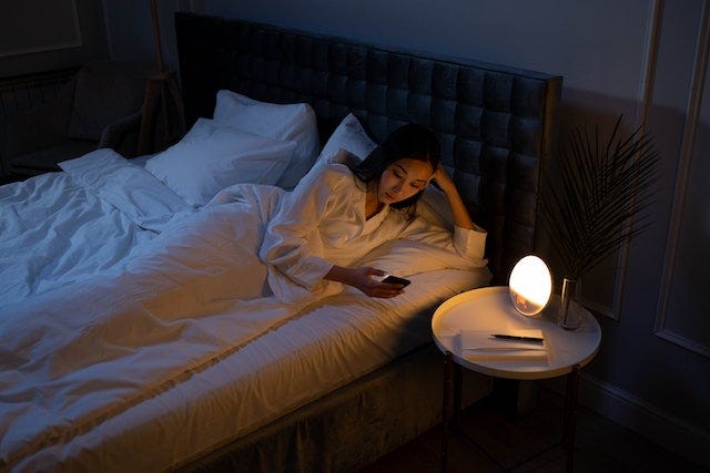 a girl lying on a bed using a mobile phone instead of sleeping