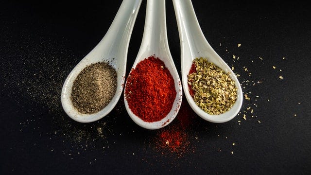 Three white tablespoons filled with assorted spices.