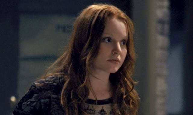 A teenager with red hair wearing black clothing stares offscreen