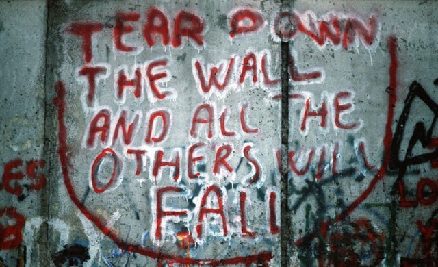 Photo of a part of the berlin wall. There is grafitti saying “Tear down the wall and all the others will fall”