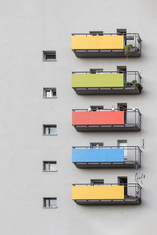 A building with vertically aligned, fenced balconies, with privacy covers in different colors