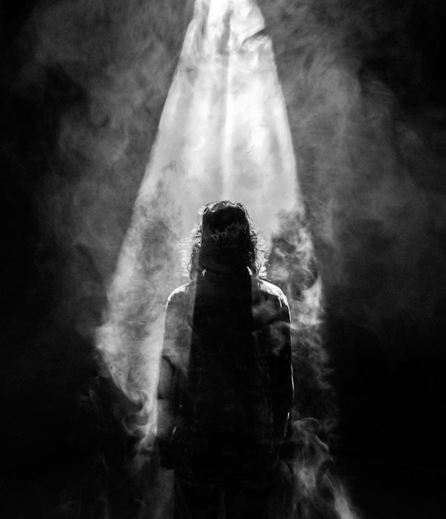 A spotlight shined on a dark outline of an individual, shadowed by smoke.