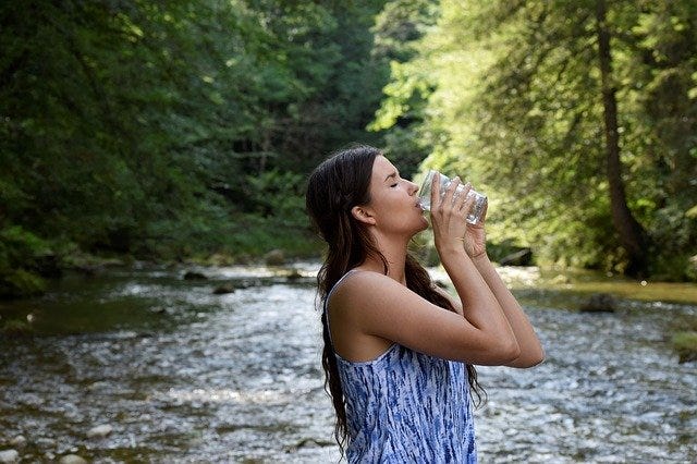 Woman drinking water in forest, woman drinking water near natural fall