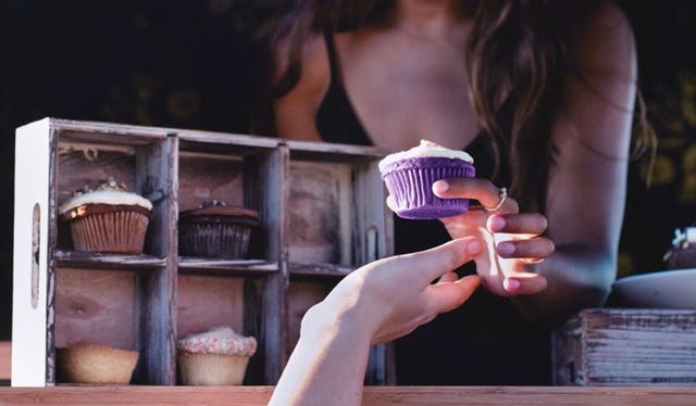Women offering a purple cupcake to a customer