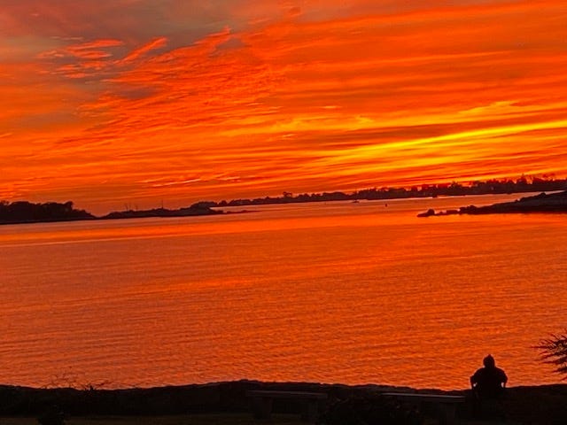 Blazing orange sunset taken from a distance with author sitting in a chair in the foreground.