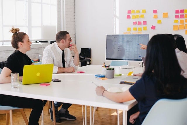 People sitting around a table looking at ideas on a computer monitor