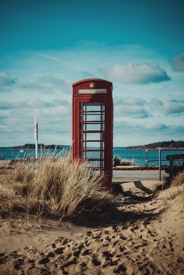 A red telephone booth standing empty in front of the shore.