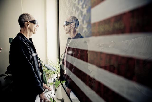 Man wearing sunglasses with his reflection in a framed USA flag