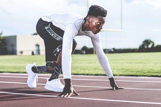 Foto de um atleta sozinho e em posição de largada sobre uma pista de corrida