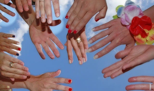 Many women hands showing off their rings together against the backdrop of a sky.