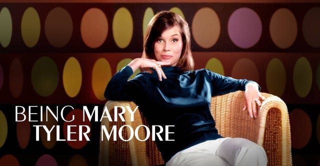 Advertisement for HBO documentary BEING MARY TYLER MOORE. Ms. Moore sits in what looks to be an oversized wicker chair. Grey slacks. Dark blue turtleneck, her right hand under her chin with a finger extended and her left hand on the arm of the chair. 1970'ish background appears superimposed behind her.