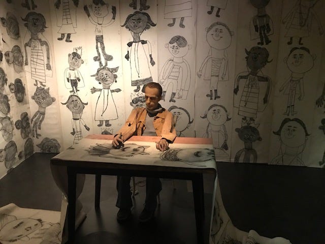 Setting with mannequin man obsessively drawing child-like drawings of children and surround by walls covered with them.