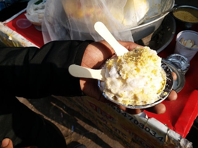 A hand cupping a paper cup filled with daulat ki chaat