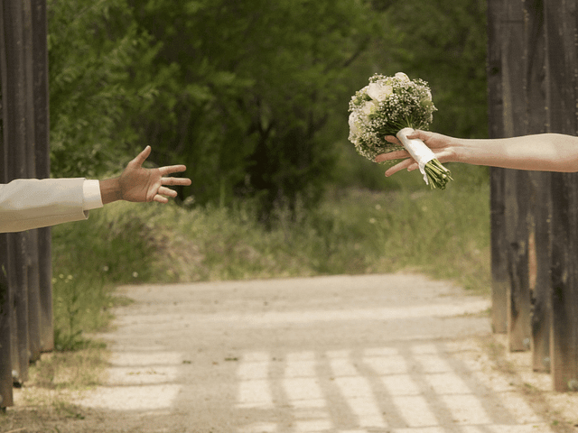 Hand of a groom and a bride holding a bouquet, stretching across a pathway. Hand/arm are different skin tones.