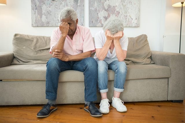 Two people sitting on a couch with their head in their hands looking really depressed