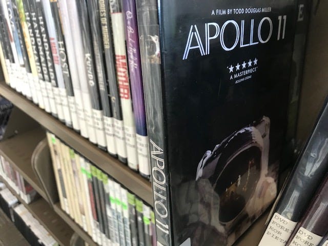 On a shelf of DVD’s, the film “Apollo 11” is selected and ready to be pulled out.
