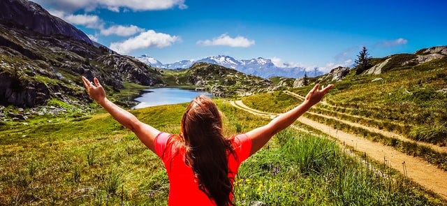 A woman with raised hands, amazed at the beauty of the lake, the mountains, the grass and the blue sky. This picture is used as a metaphor for the woman who is looking into the future. How would it be when she embraces motherhood?