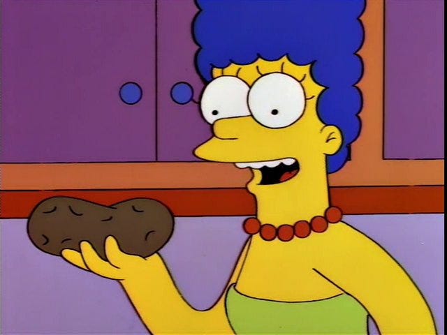 A Simpsons screenshot of Marge holding a potato and smiling.