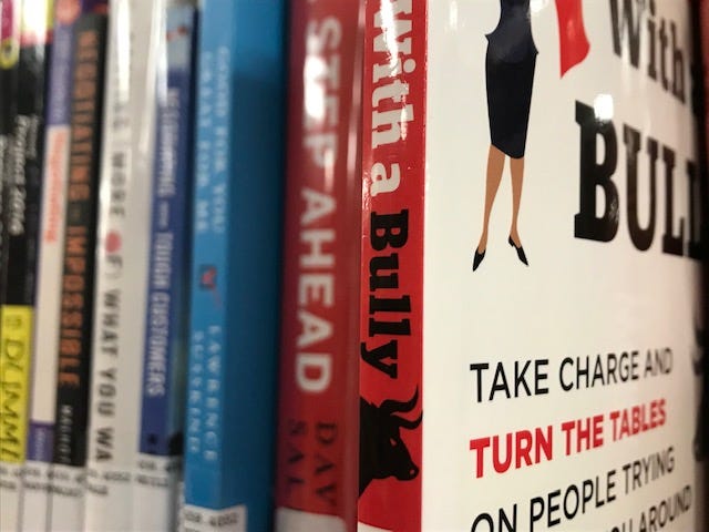 A group of books on a shelf. One book, with the word “bully” on it is selected and is ready to be pulled off the shelf.