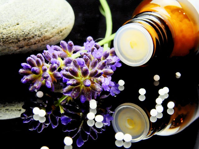 A table covered in objects — an oil bottle knocked over, purple flowers, a rock. little round orbs spilled across the table.