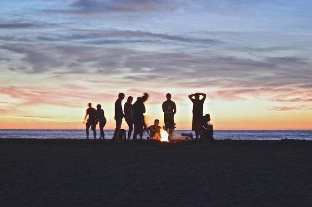People hanging out around a fire by the beach at sunset.