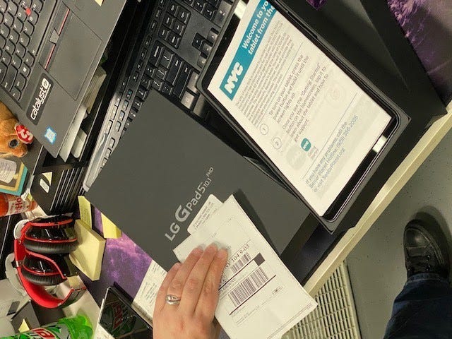 A desk with kitting materials is shown, including a printed mailing address with a barcode scanner and LG tablet box.