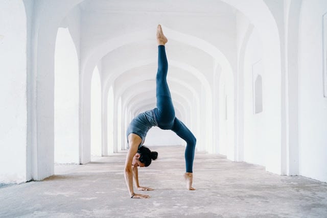 Woman in a blue with a white background doing a difficult yoga pose effortlessly