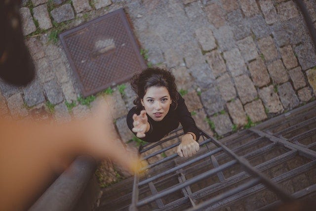 a woman at the bottom of a ladder reaching for a hand for help