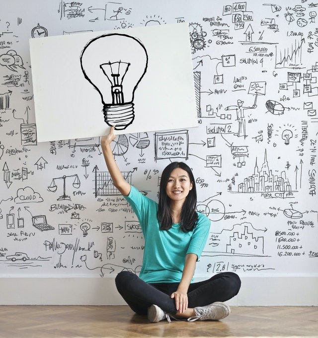 A sitting girl holding a sheet in her hand with an idea sign drawn on it.