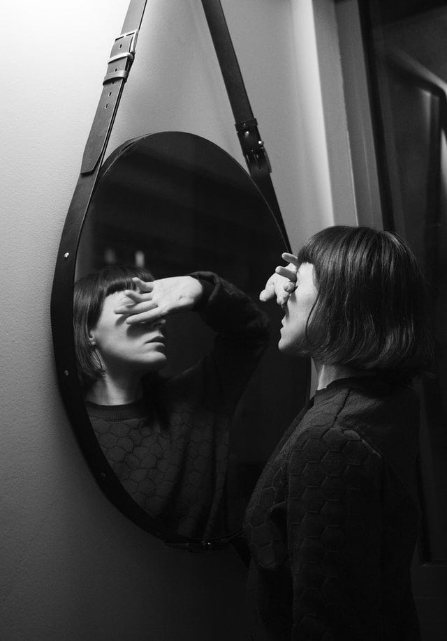 Women reflected in a mirror; her hand covers her eyes