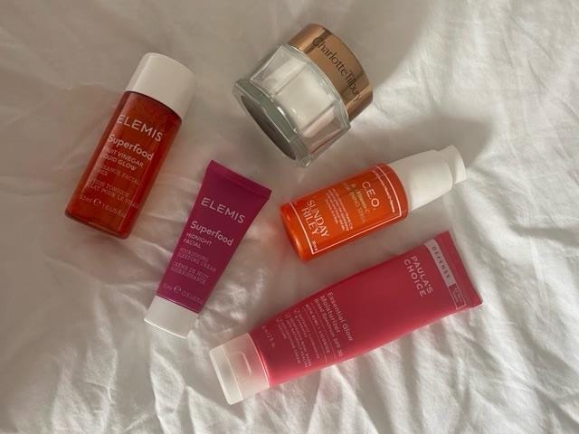 Image shows 5 skincare products on a white sheet. There is a superfood liquid glow by Elemis in an orange bottle, a small pink bottle by Elemis saying ‘Midnight glow’, Sunday Reiley’s ‘CEO glow’ in an orange bottle and Paula’s Choice’s SPF in a tall pink bottle