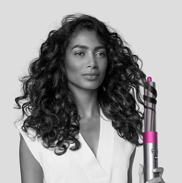 A black and white photo of a woman with curly hair holding Dyson Airwrap Styler.