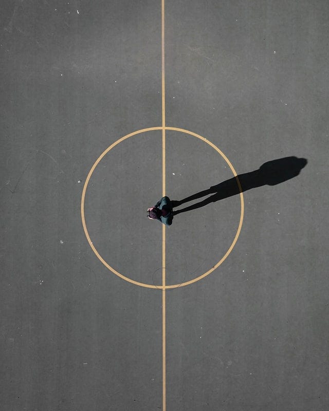 Image from above of a man standing in the middle of the centre circle of an asphalt basketball court