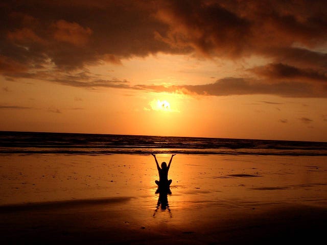 person sitting on a beach with arms raised at sunset