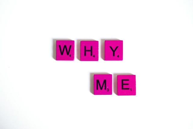Pink colored tiles with black lettering spelling out “why me”