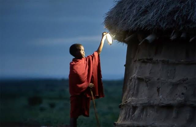 Boy holding lantern up against thatched roof of a hut