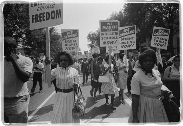 A photo of Black women marching with signs for equal rights, integrated schools, decent housing, and an end to bias.