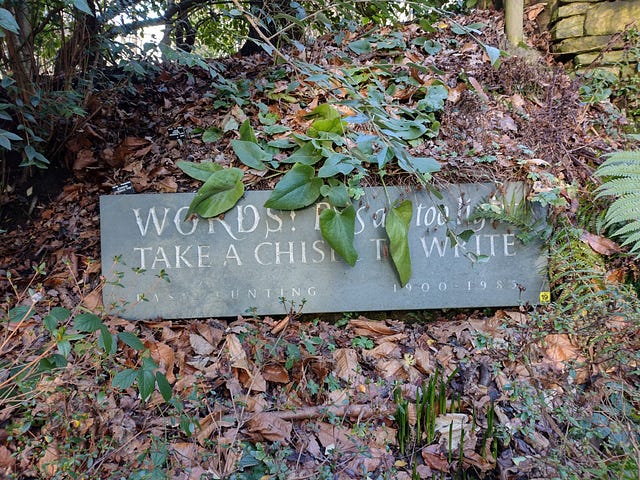 A sign over some leaves that read: “Words! Pens are too light. / Take a chisel to write.”