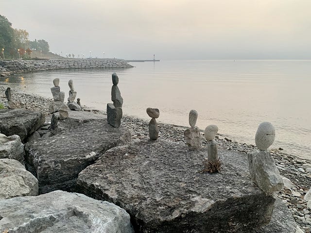 a calming scene of the sunrise by the waterfront, with stacked stones by the lakeshore