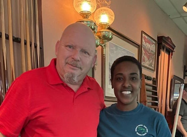Teammates, Amani and Doug, stand in a pool hall posed for a picture