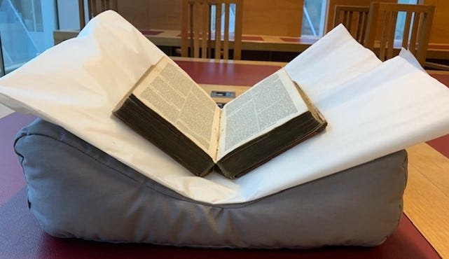 An open book with a leather cover which has red rot, supported on a book cushion which has been covered with acid free tissue to protect the cushion from red rot staining