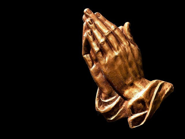 A pair of gold hands clasped together in prayer.