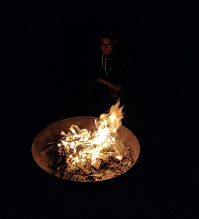 Person sitting behind a fire, looking into the fire.
