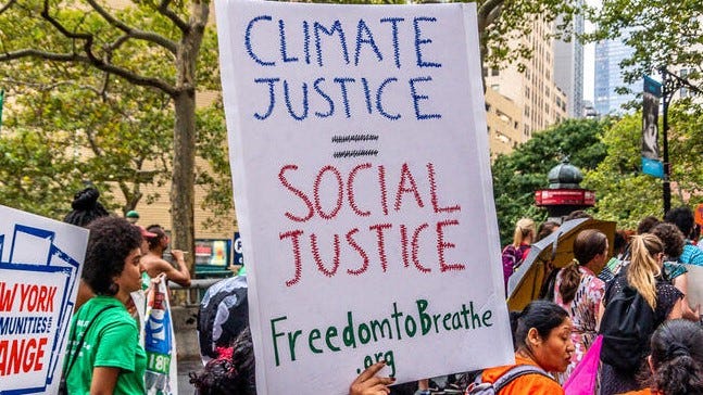 Sign at a rally with the words “CLIMATE JUSTICE = SOCIAL JUSTICE” written in blue, red, and black.